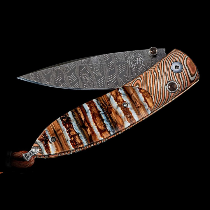 A close-up of a pocket knife with the blade halfway angled to the left. The pocket knife features a twisted Mokume gane frame, inlaid 10,000-year-old fossil Woolly Mammoth tooth, and ‘Hornets Nest’ damascus steel blade.