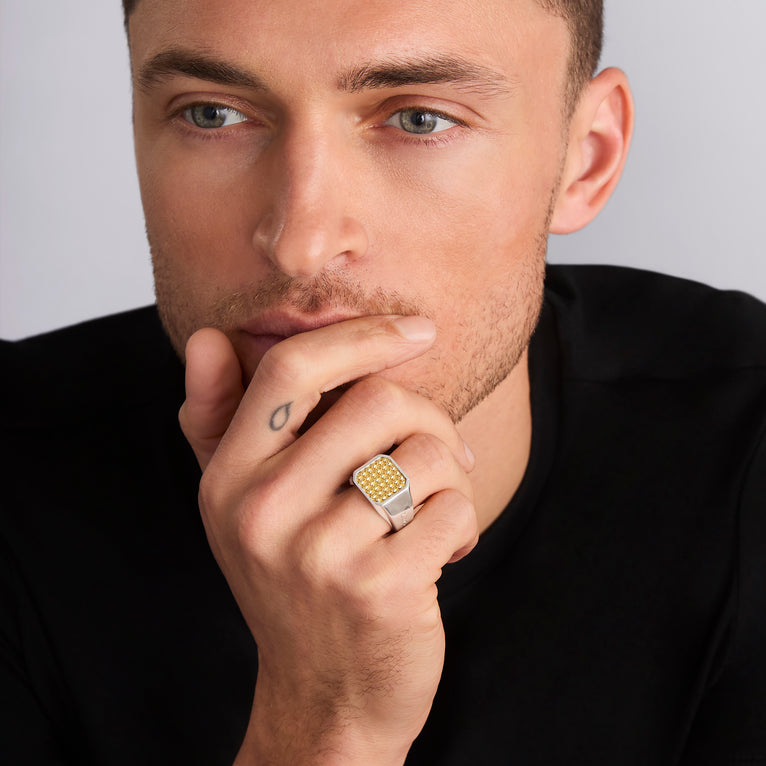 A man is wearing a sterling silver and 18k gold ring featuring 18K gold Caviar beading surrounded by smooth sterling silver with a square design.