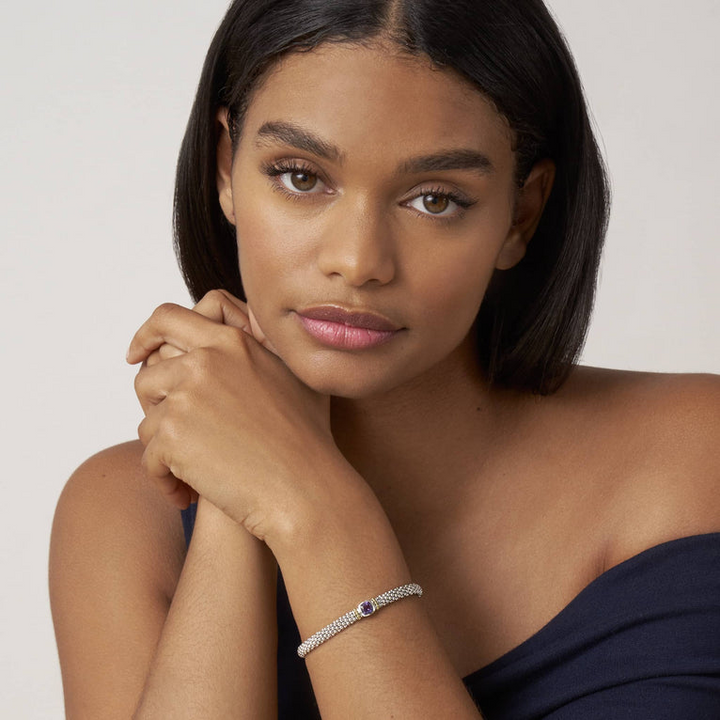 A woman wearing a sterling silver bracelet in the middle of a white background features an amethyst gemstone and sterling silver Caviar beading with 18K gold detailing.