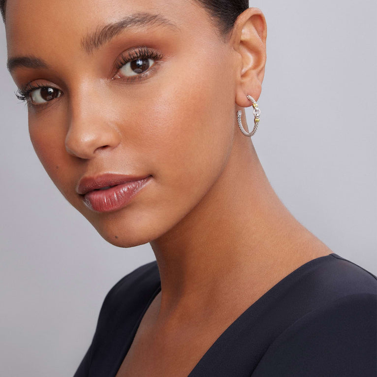 A woman is wearing a black top and a pair of hoop earrings made from Sterling silver Caviar, with a circle motif and 18K gold accents. 