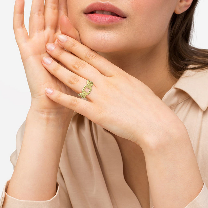 A close-up of a woman with brown hair wearing a tan blouse and a yellow gold ring around her ring finger. The ring features 18K gold variations of Caviar beading and fluting elements, and an oval link design.