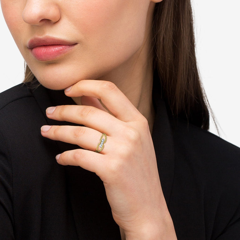 A close-up of a woman with brown hair, wearing a black blouse and a yellow gold ring around her ring finger. The ring features 18k gold superfine Caviar beading and four round-shaped diamonds set in the middle of the two gold loops, all set in 18k White Gold.