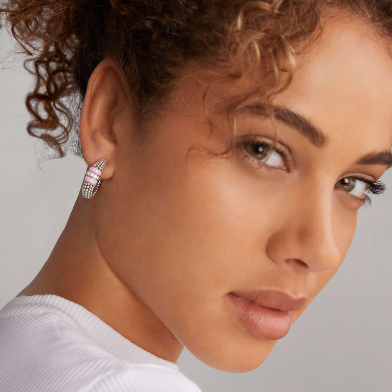 A woman wearing a pair of hoop earrings with pink ceramic and a diamond station with sterling silver Caviar beads. 