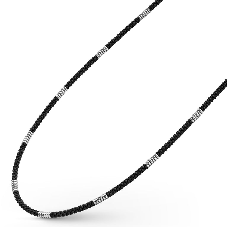 A sterling silver and ceramic beaded necklace angled to the right in the middle of a white background featuring matte black ceramic and silver Caviar beading.