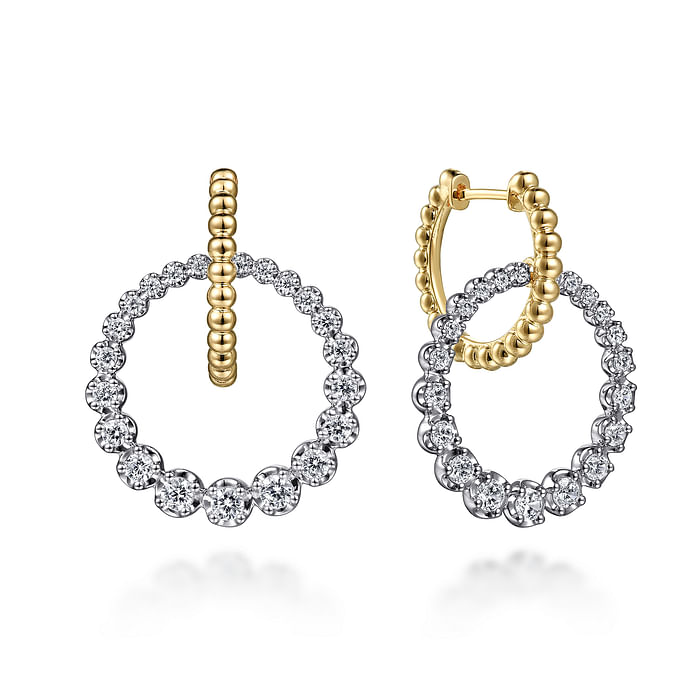 Huggie drop earrings with a circular motif combine 14K yellow gold and diamonds. The right earring is angled to the side.