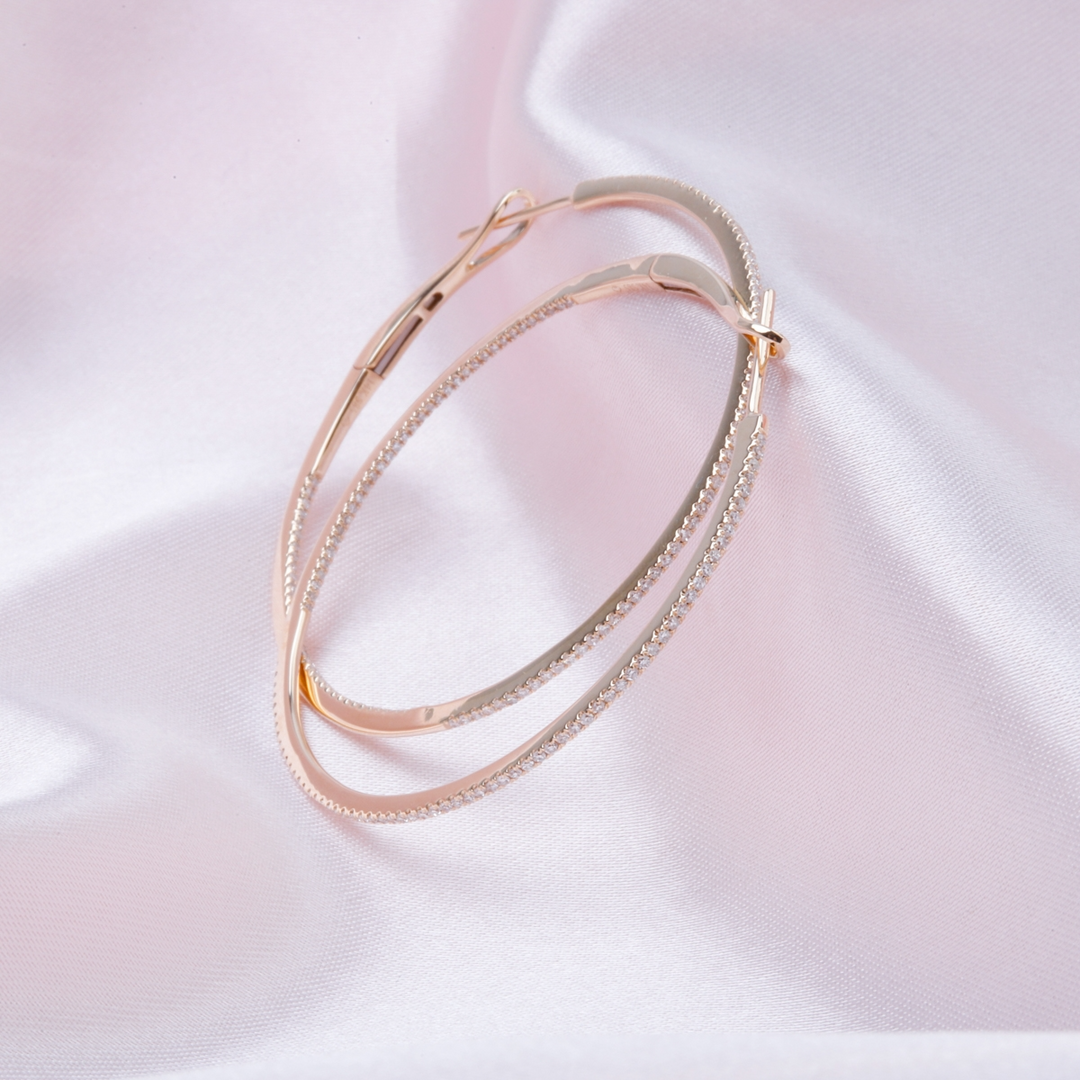 A pair of yellow-gold hoop earrings with a single row of round diamonds resting against a light pink background.