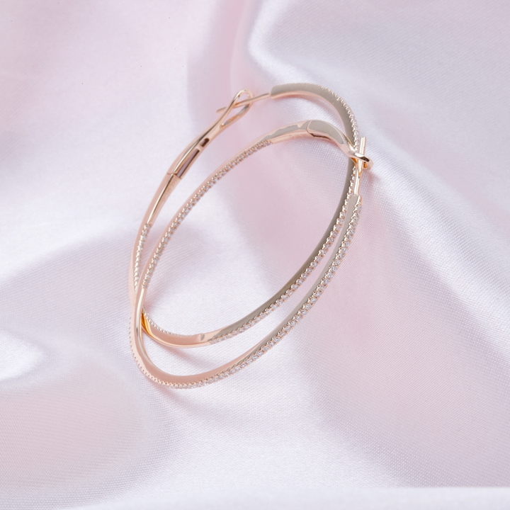 A pair of yellow-gold hoop earrings with a single row of round diamonds resting against a light pink background.