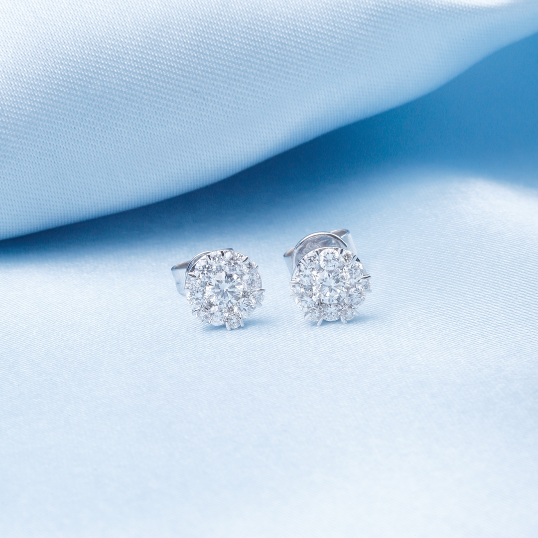 A pair of stud earrings with mixed-sized diamonds rests against a light-blue background