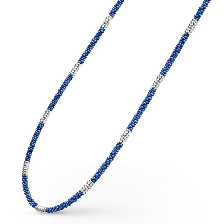 A sterling silver and ceramic beaded necklace angled to the right in the middle of a white background featuring blue ceramic and silver Caviar beading.