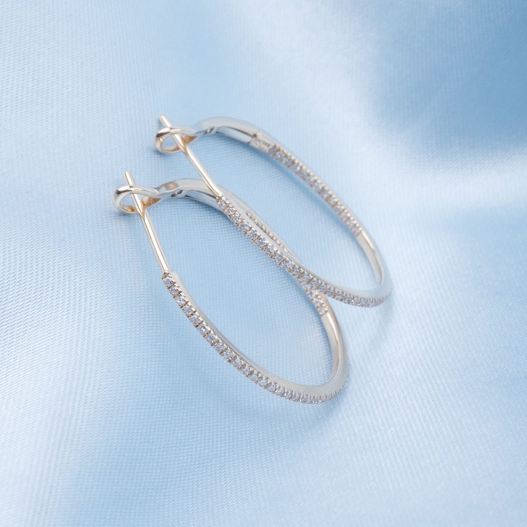 A pair of hoop earrings with a single row of round diamonds rests against a light blue background.