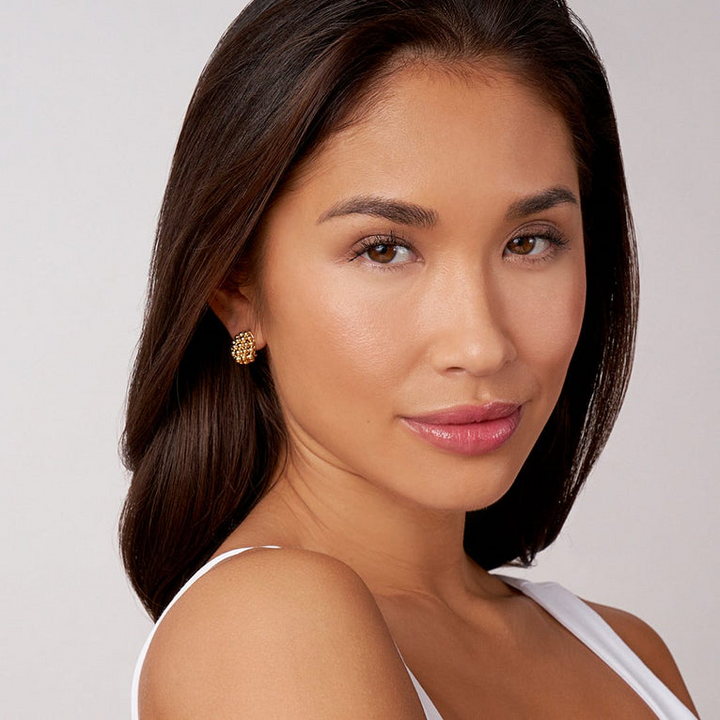 A woman is wearing a white tank top and a pair of omega clip earrings with gold caviar beading. 