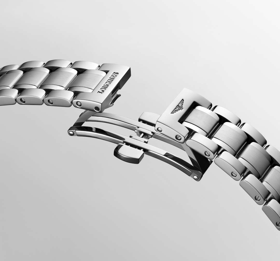 A close-up of a Longines watch angled showing the stainless steel bracelet and undone clasp. The Longines logo is engraved the clasp.