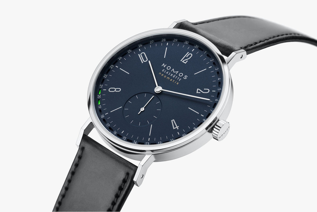 A side view of a Nomos Glashutte watch angled & curved to the left. It features a blue dial, silver hands and markers, a stainless steel bezel, and a black leather strap.