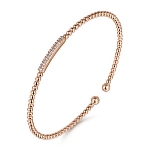 A rose-gold bangle bracelet with a beaded band, diamond set station in the middle, and end caps is angled in the middle of a white background.