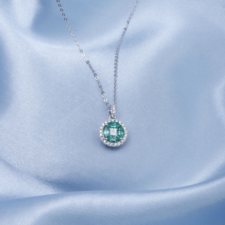 A close-up of a white-gold Marquise Necklace against a blue background. The necklace features a diamond center stone with marquise-shaped emerald diamonds and round diamonds.