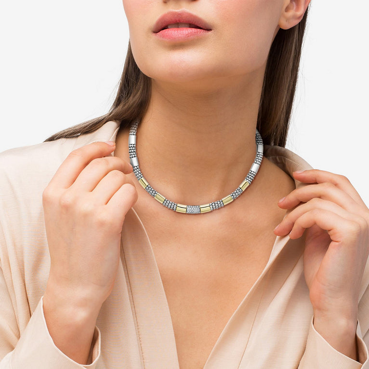 A close-up of a woman wearing a sterling silver &18k gold necklace featuring round diamonds and smooth stations of 18K gold and sterling silver surrounded by Caviar beading.