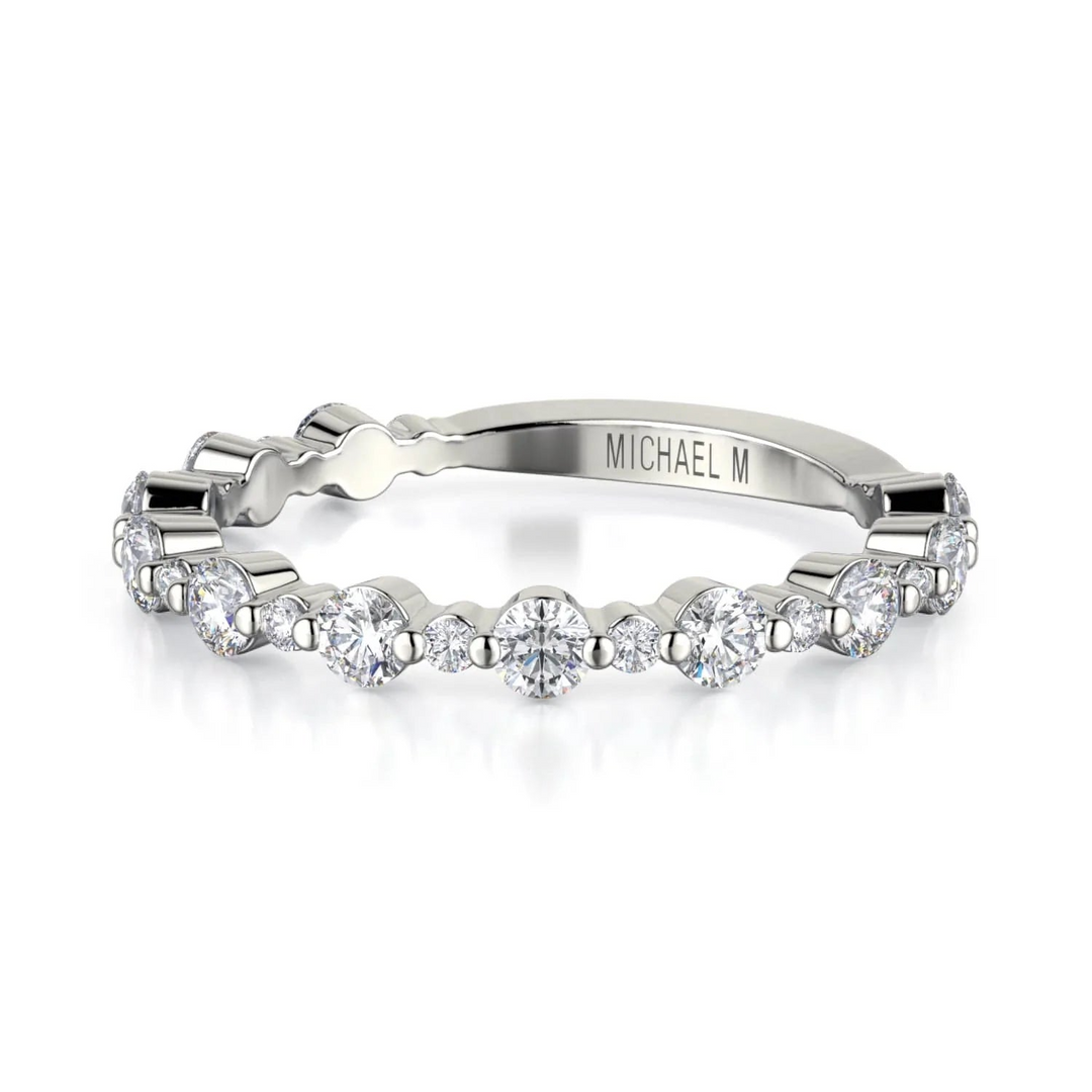 A white gold ring lies flat against a white background. The ring features round-cut diamonds with an alternating pattern of larger and smaller gemstones. The inscription of "MICHAEL M" is visible on the band.