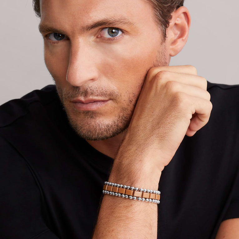 A man is wearing a stainless steel bracelet featuring matte tan ceramic and caviar beading.