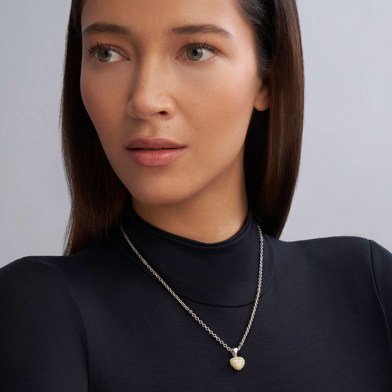 A close-up of a woman wearing a sterling silver &18k gold necklace featuring a diamond heart pendant framed by 18K Gold Caviar beading