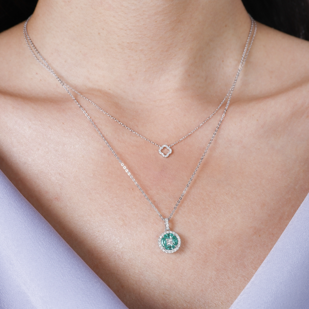 A woman is wearing a white-gold Marquise Necklace and a purple top. The necklace features a diamond center stone with marquise-shaped emerald diamonds and round diamonds.