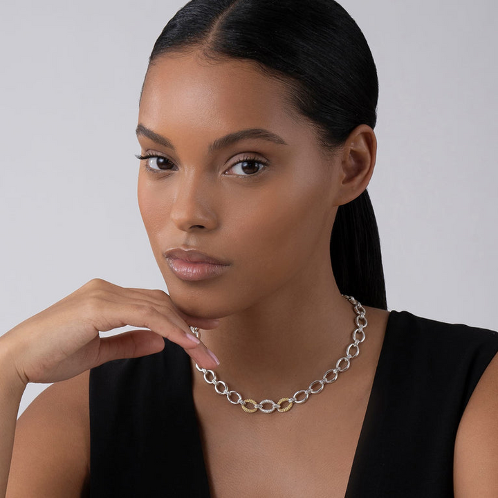 A close-up of a woman wearing a sterling silver &18k gold necklace featuring a pave diamond link, caviar beading, and a lobster clasp.