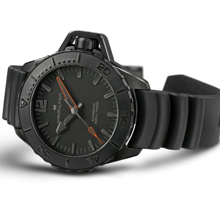 A Hamilton watch is lying on its left side against a white background. It features a black dial, white hands and markers, a PVD black coating steel case, a steel bezel, a steel crown, and a rubber strap.