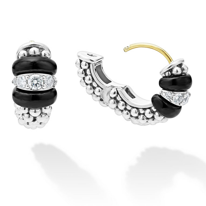 A pair of huggie earrings with smooth black ceramic and diamonds with Caviar beading. The right earring is angled to the side and unclasped.