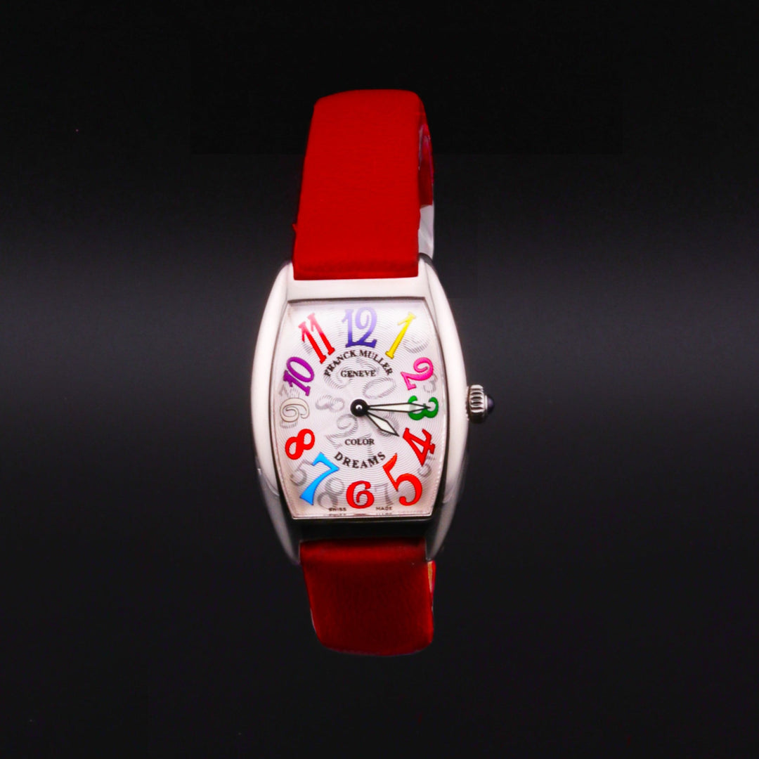 This is a close-up of a Frank Muller watch. The watch features a white with black numbers faded dial, a steel case and crown, multicolored hands and markers, and a red leather strap on a black background.