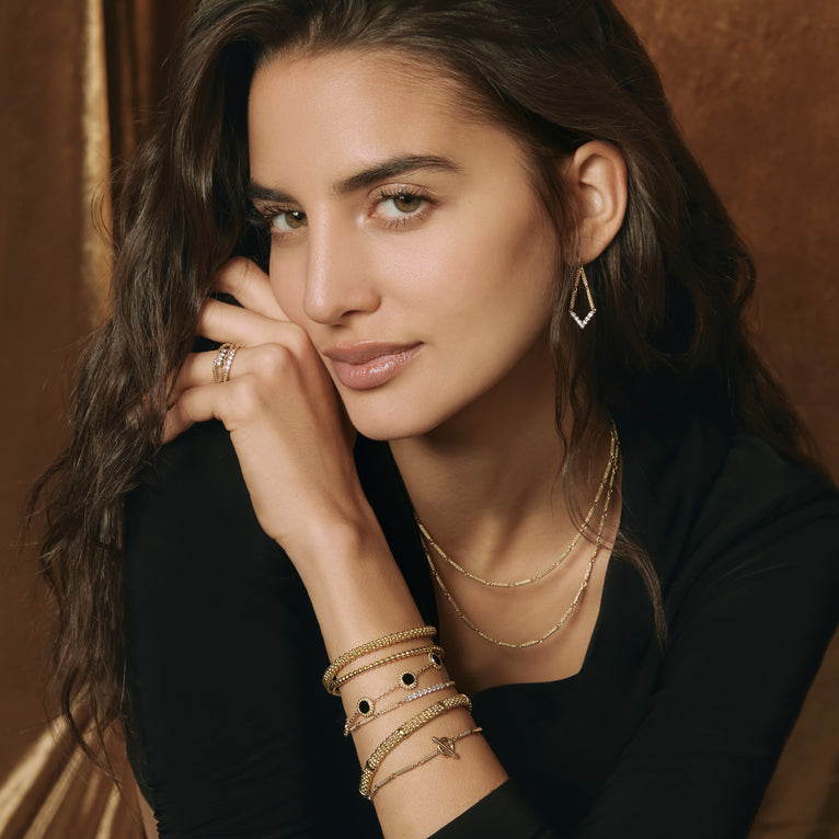 A woman is wearing a black top and other accessories, including a pair of drop earrings with diamonds set in chevron-shaped motif and superfine caviar beading. 