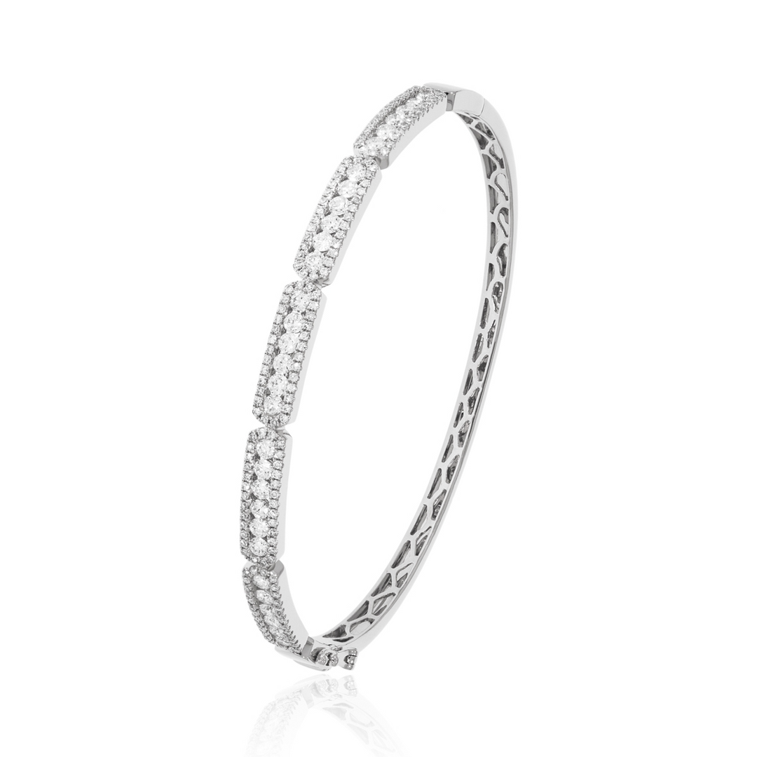 A bangle bracelet angled in the middle of a white background is made of 14k white gold and features a pave diamond cluster design.