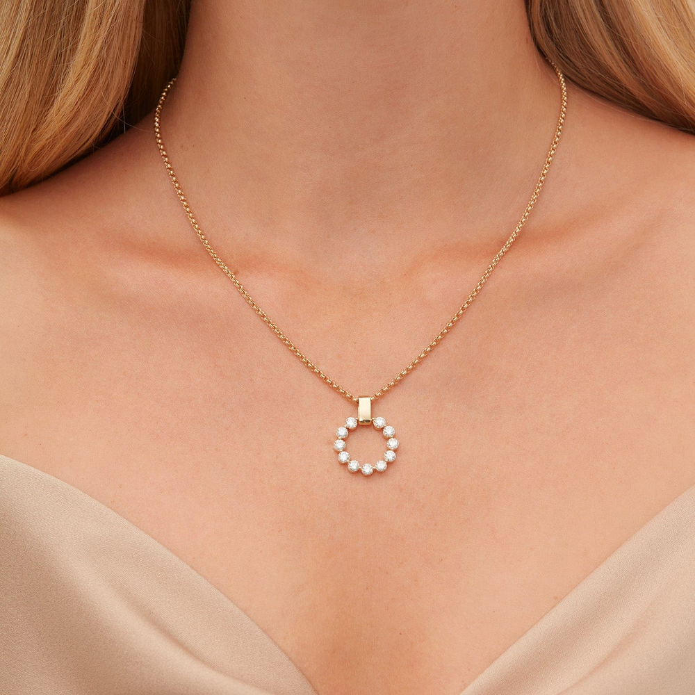 A close-up of a woman wearing a yellow-gold necklace. The bracelet features a circle pendant and a smooth gold bar with a belcher chain.