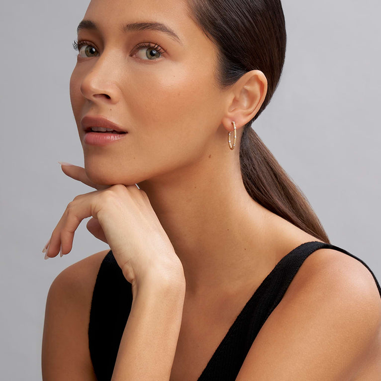 A woman is wearing a black tank and hoop earrings with diamonds accented with 18k gold superfine Caviar beading.