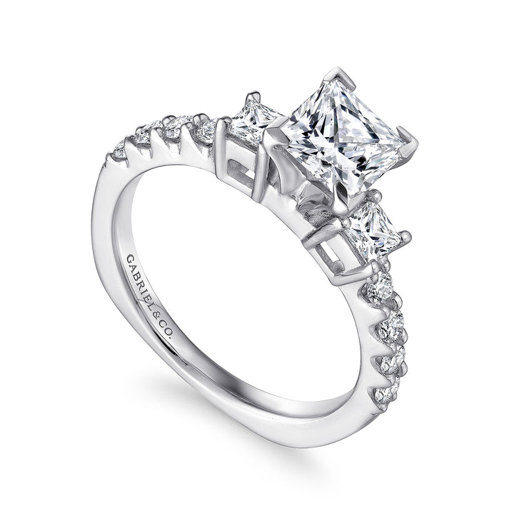 A close-up of the Princess Cut Three Stone Diamond Engagement Ring, made of white gold, angled to the right against a white background. It features a three-stone center diamond.