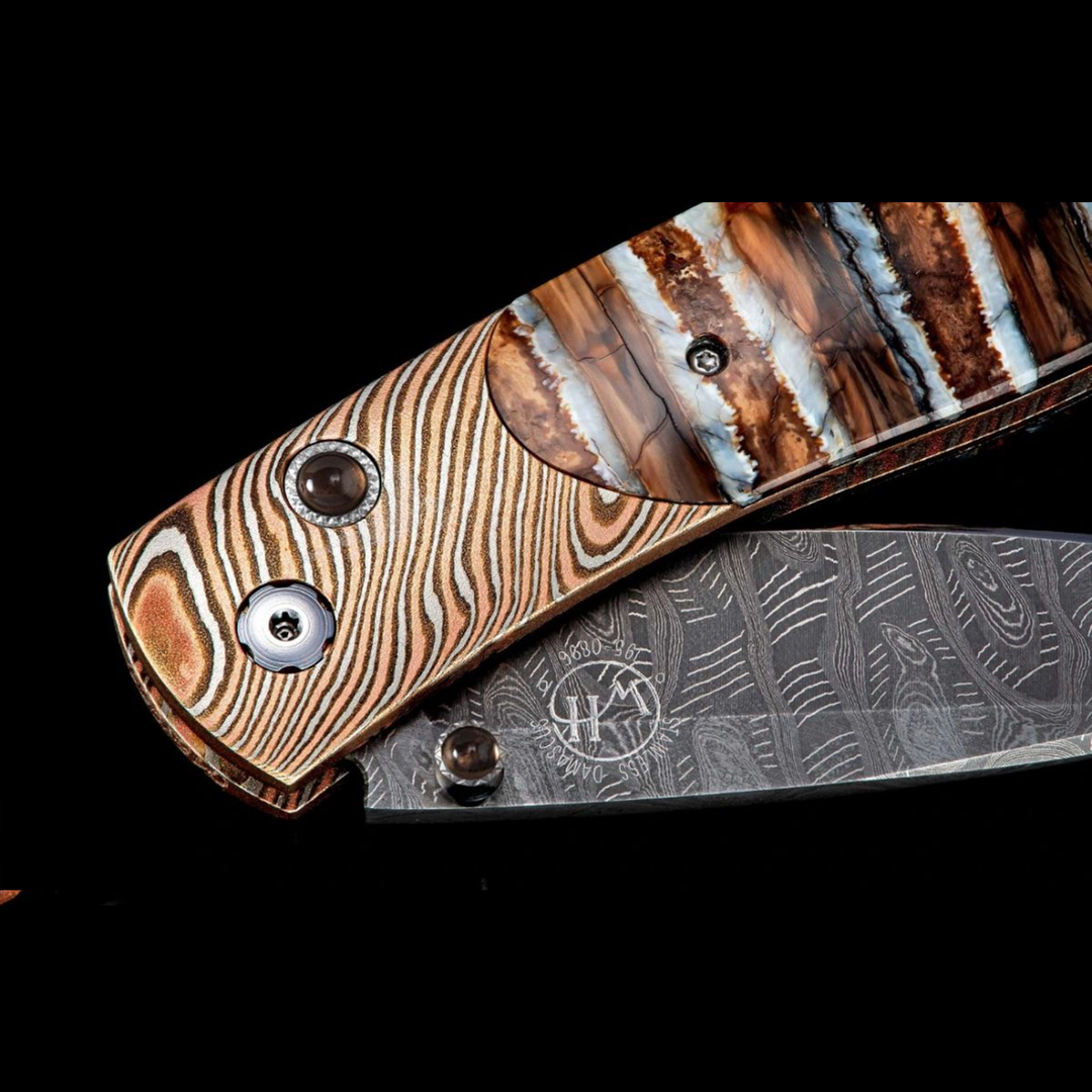 A close-up of a pocket knife with the blade halfway angled to the right. The pocket knife features a twisted Mokume gane frame, inlaid 10,000-year-old fossil Woolly Mammoth tooth, and ‘Hornets Nest’ damascus steel blade.