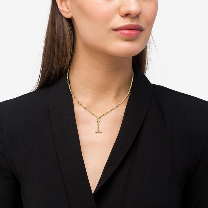 A close-up of a woman wearing an 18k gold necklace featuring caviar beading and a toggle clasp. against a white background.