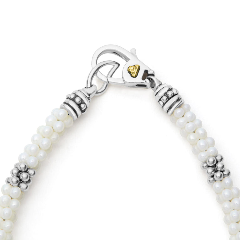 A sterling silver and ceramic beaded bracelet standing vertically in the middle of a white background featuring white ceramic and silver Caviar beading.