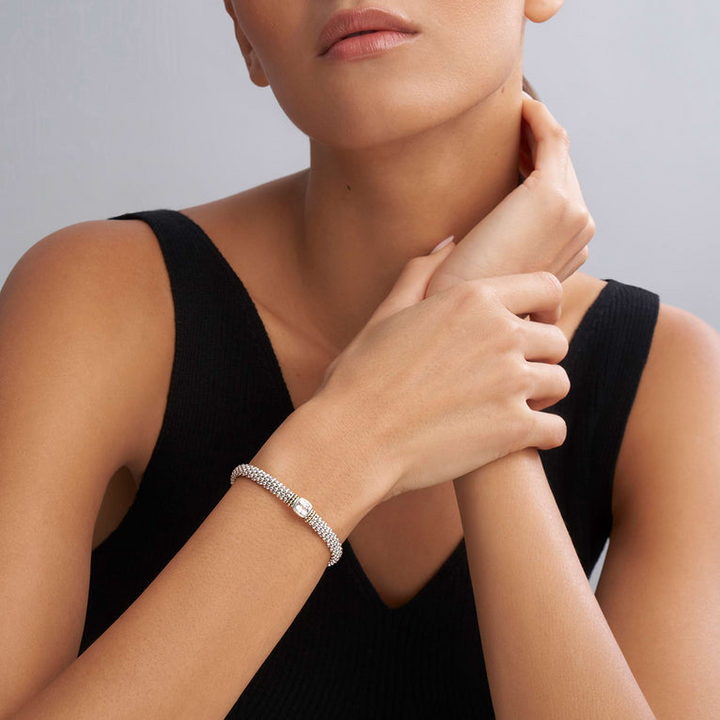 A woman wearing a sterling silver bracelet in the middle of a white background features a white topaz gemstone and sterling silver Caviar beading with 18K gold detailing.