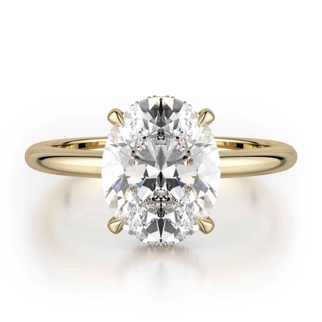 The Hidden Halo Solitaire Engagement Ring, made of yellow gold, lies flat against a white background. It features an oval-cut diamond set in the center with a diamond set hidden halo