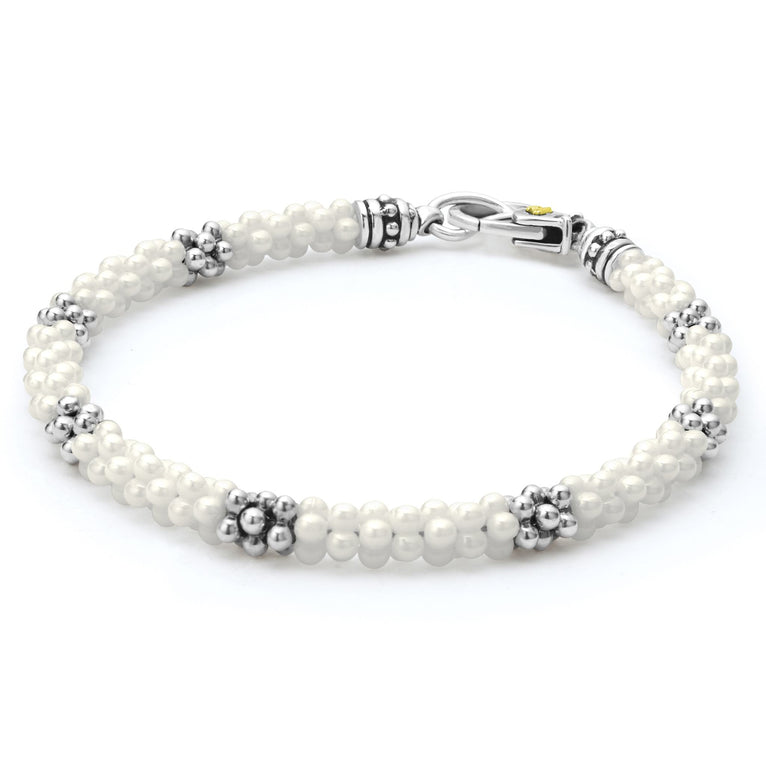 A side-view of a sterling silver and ceramic beaded bracelet in the middle of a white background featuring white ceramic and silver Caviar beading.