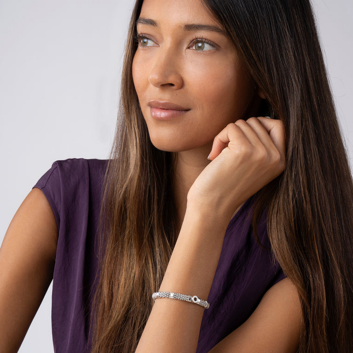 A woman is wearing a sterling silver bracelet featuring one diamond circle station and caviar beading.