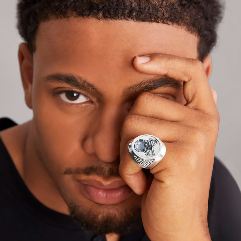 A man is wearing a sterling silver ring featuring a skull motif on the signet ring