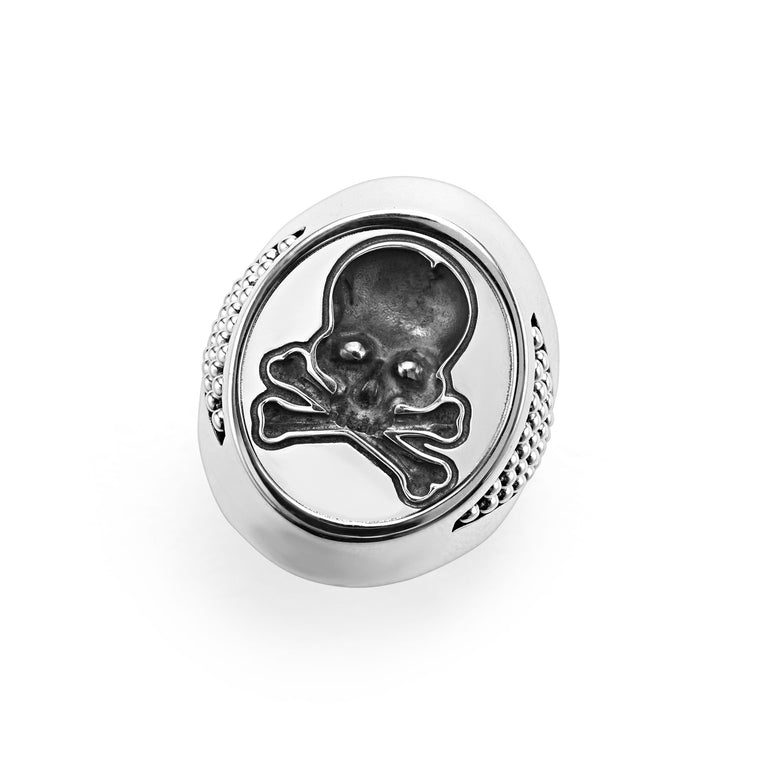 A sterling silver ring angled to the right in the middle of a white background featuring a skull motif on the signet ring