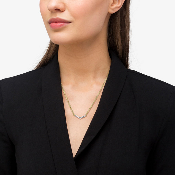 A close-up of a woman wearing an 18k gold necklace featuring caviar beading and a white gold chevron design against a white background.