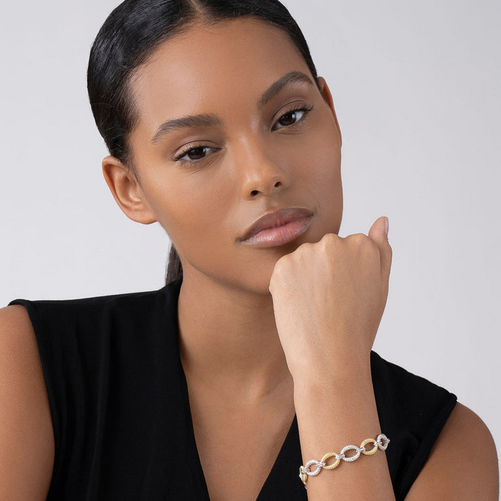 A close-up of a woman wearing a black top and a Sterling Silver & 18k gold bracelet. The bracelet has pave diamond links and a signature lobster clasp. 