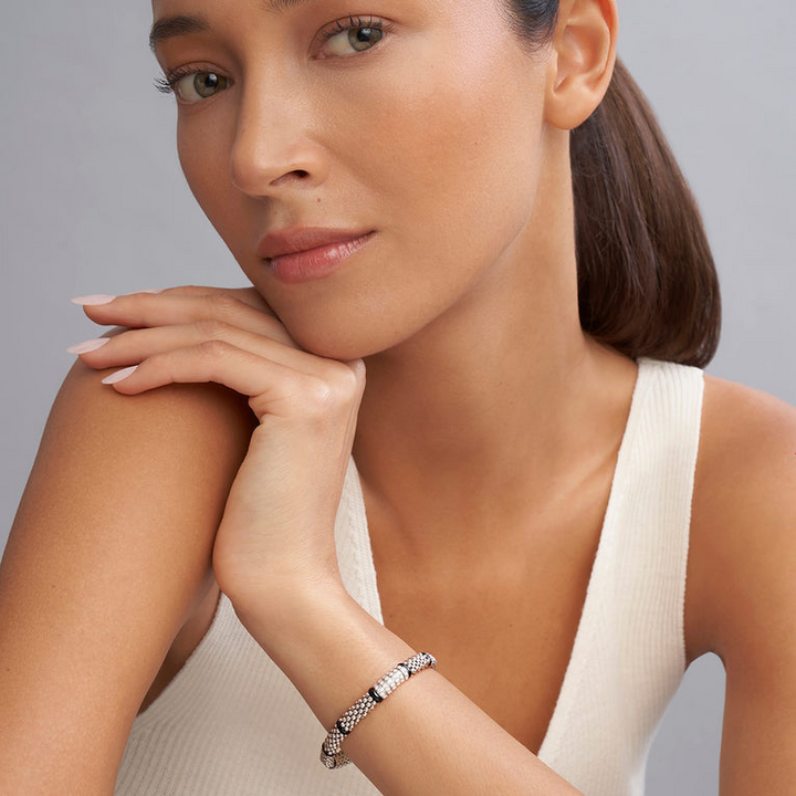 A woman wearing a sterling silver bracelet in the middle of a white background features smooth black stations, diamond-set stations, and ceramic caviar beading.