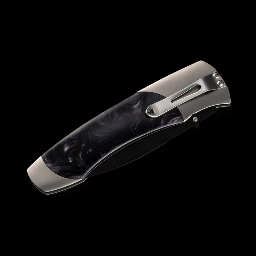 A close-up of a pocket knife with the blade in the case. The pocket knife features an aerospace-grade titanium frame, inlays of compressed acrylic resin with an inset engraving plate, and a three-layer billet blade.