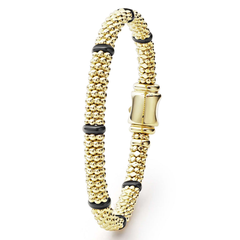 An 18k gold bracelet is angled to the side in the middle of a white background. The bracelet features smooth black stations and caviar beading.