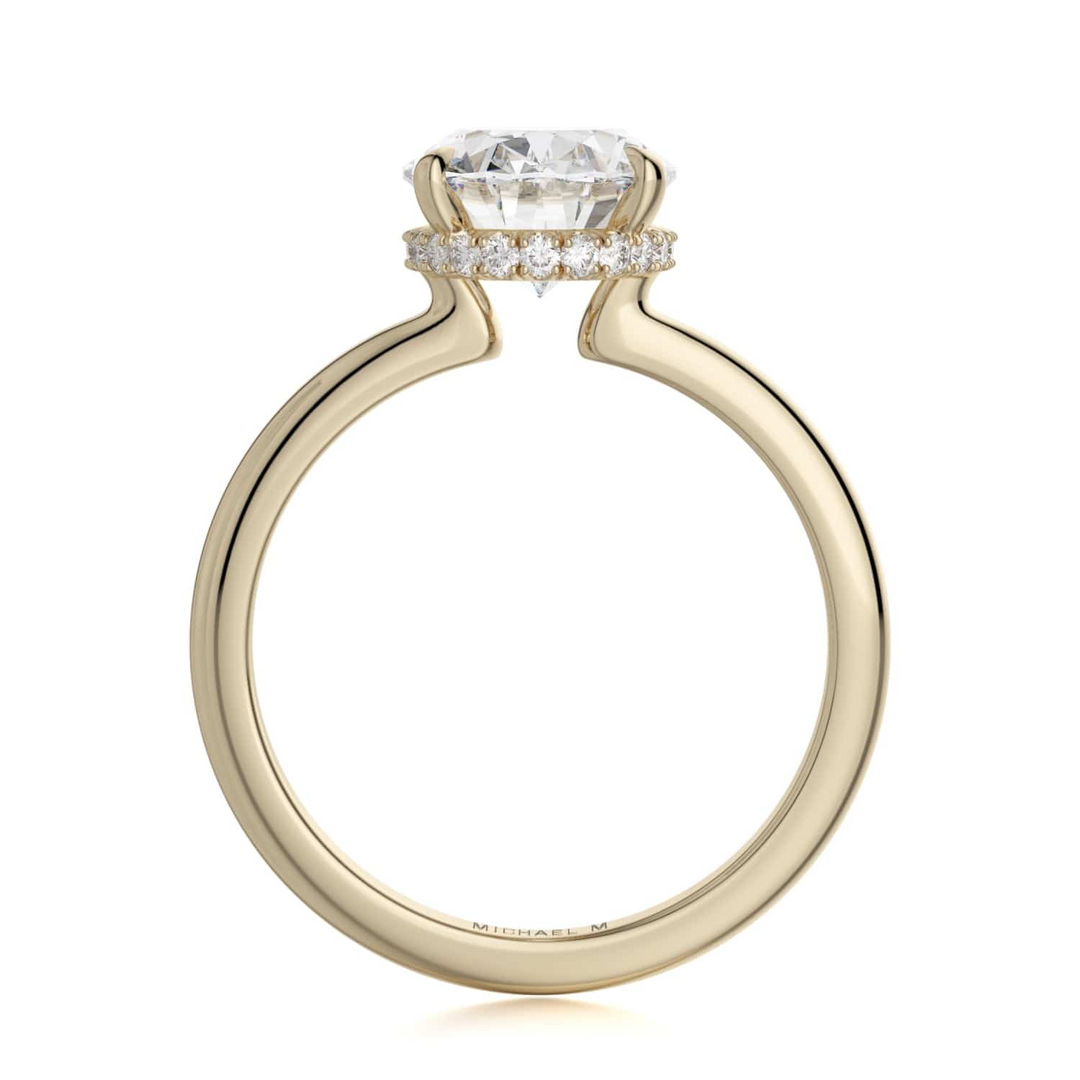 A side-view of the Hidden Halo Solitaire Engagement Ring, made of yellow gold. The side view shows the diamond's pavilion and the whole yellow-gold band. Showing the "Michael M" inscription is visible inside the band at the bottom.