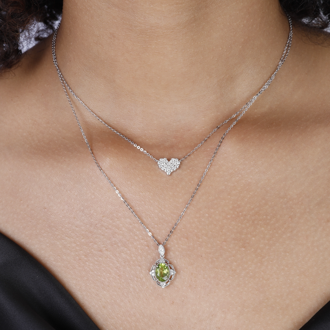 A close-up of a woman wearing a white-gold Diamond Cluster Heart Necklace and a black top. The necklace features a heart design with a cluster of round diamonds.