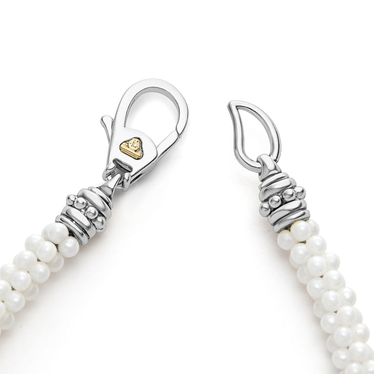 A sterling silver & 18k gold bracelet focusing on the clasp of a white background featuring five sterling silver stations and white ceramic caviar beading.